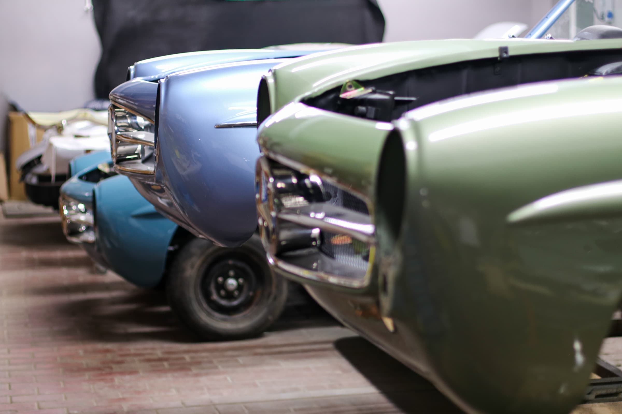The fronts of three Mercedes-Benz 190SL roadsters, in green, silver-blue and pale blue, lined up in the Oldtimer Studio workshop during restoration